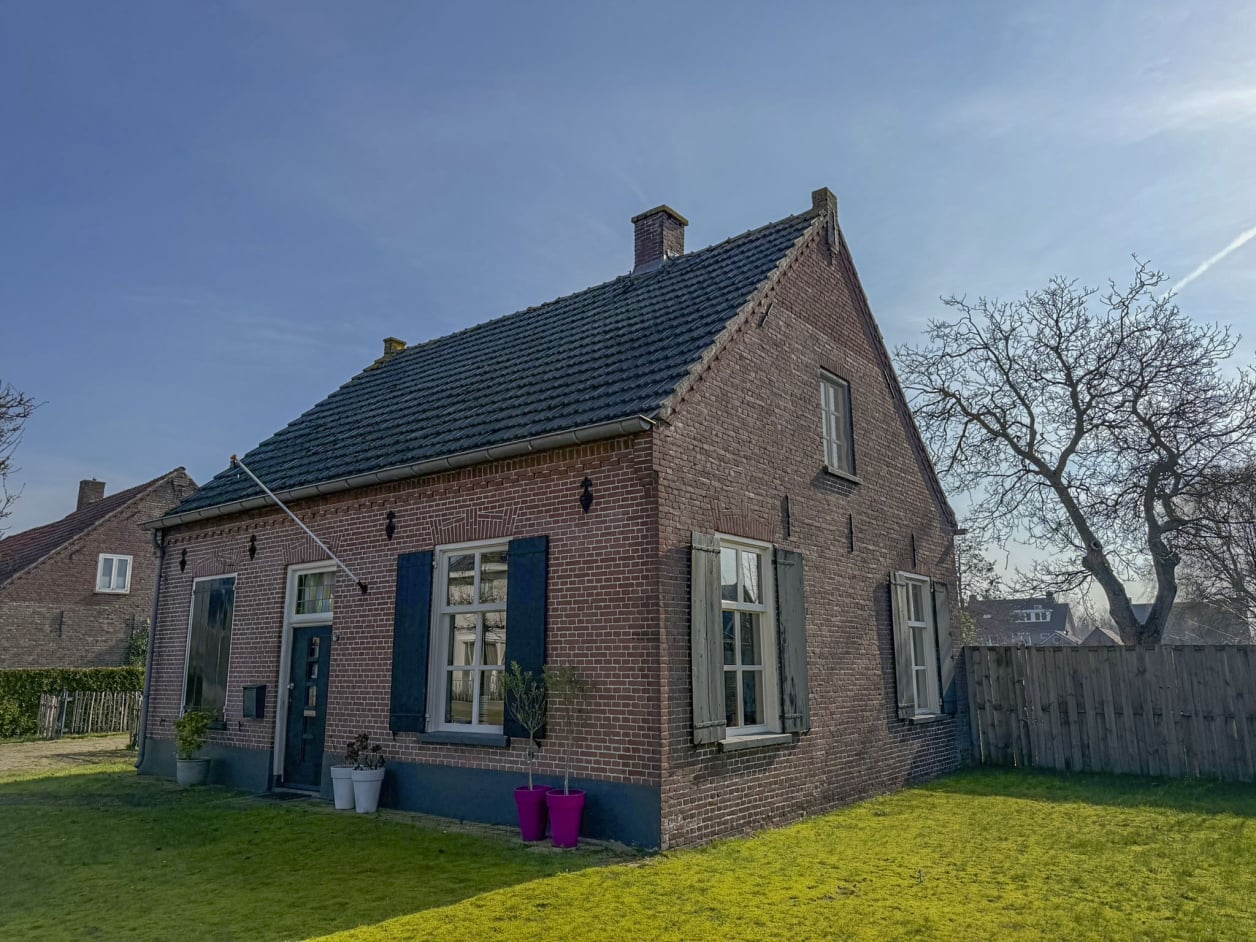 Foto van een landelijke woning met metselwerk en een zadeldak. De ramen hebben klassieke luiken