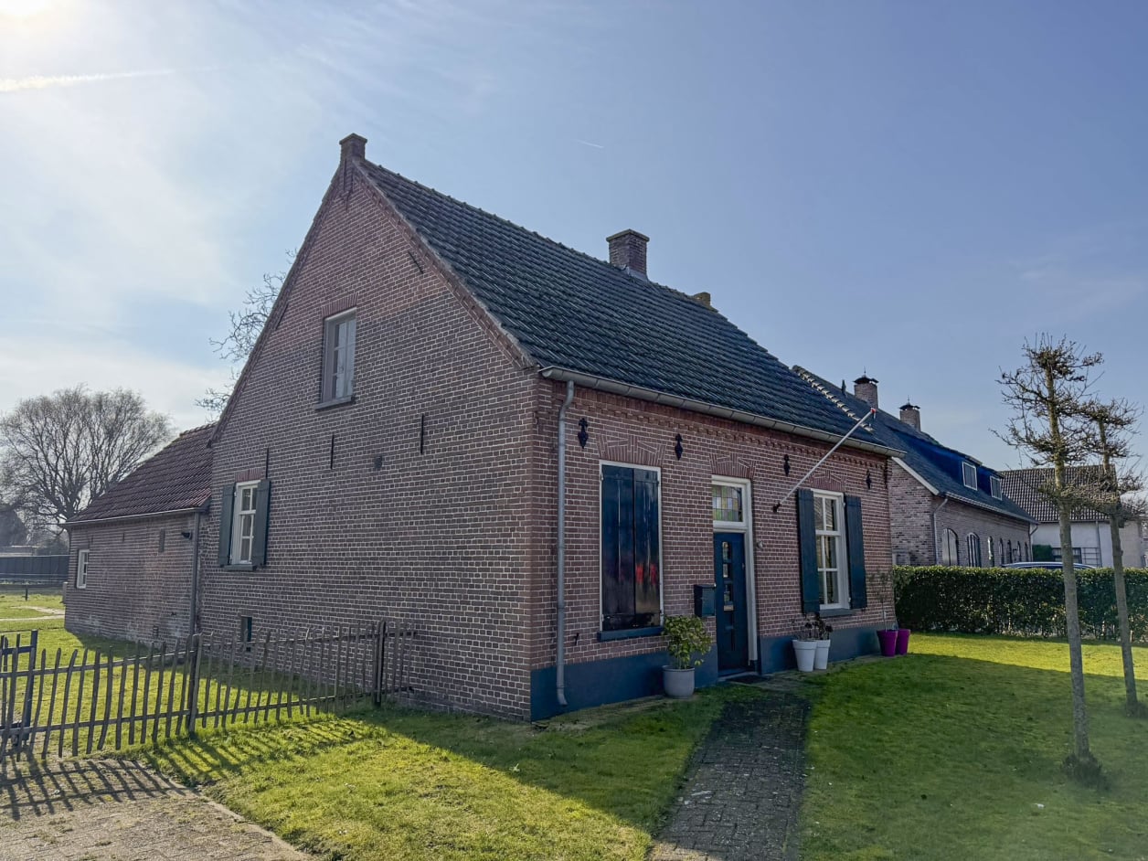 Foto van een landelijke woning met metselwerk en een zadeldak. De ramen hebben klassieke luiken